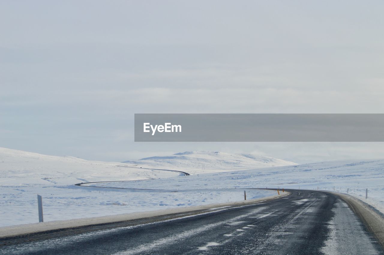 ROAD BY SNOWCAPPED MOUNTAINS AGAINST SKY