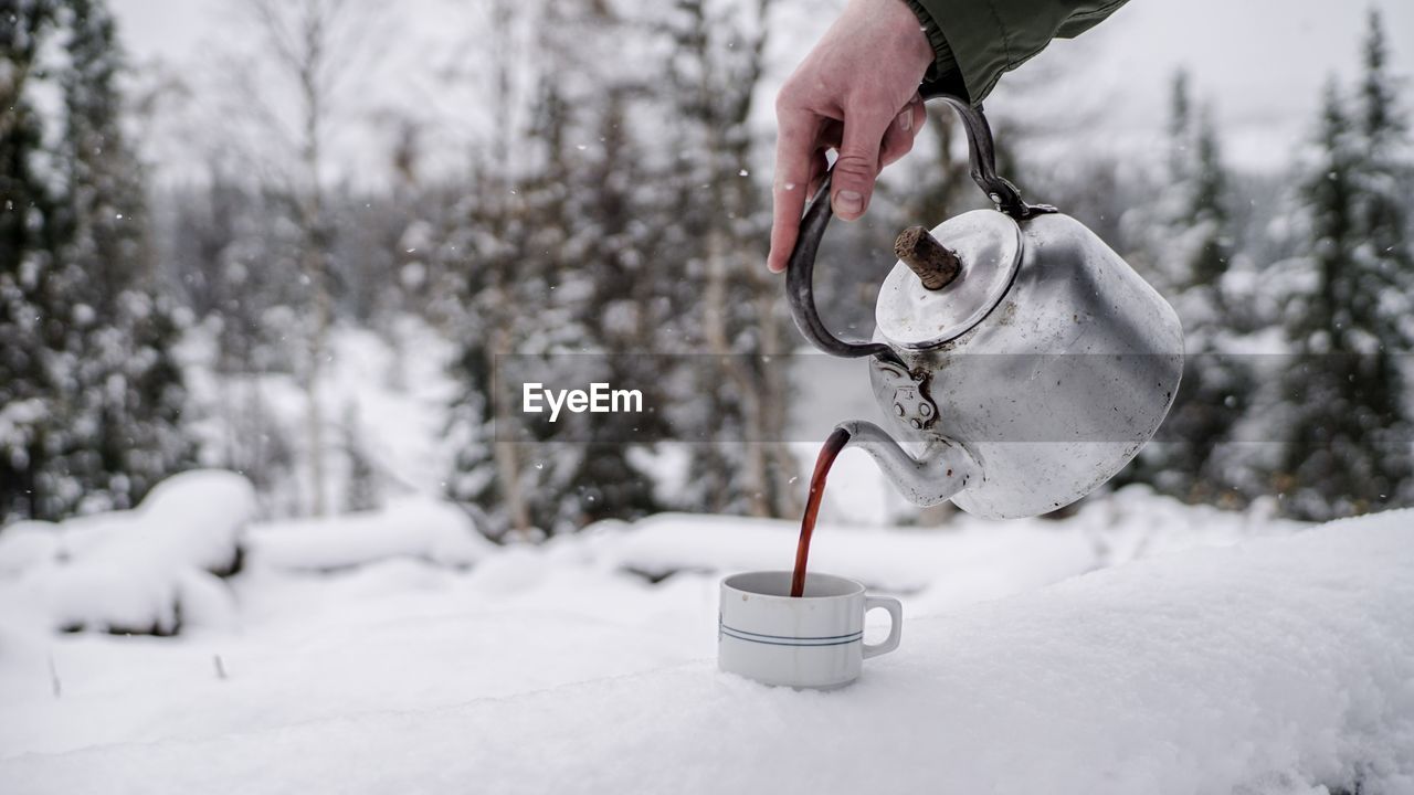 Cropped hand of person pouring tea in cup on snow