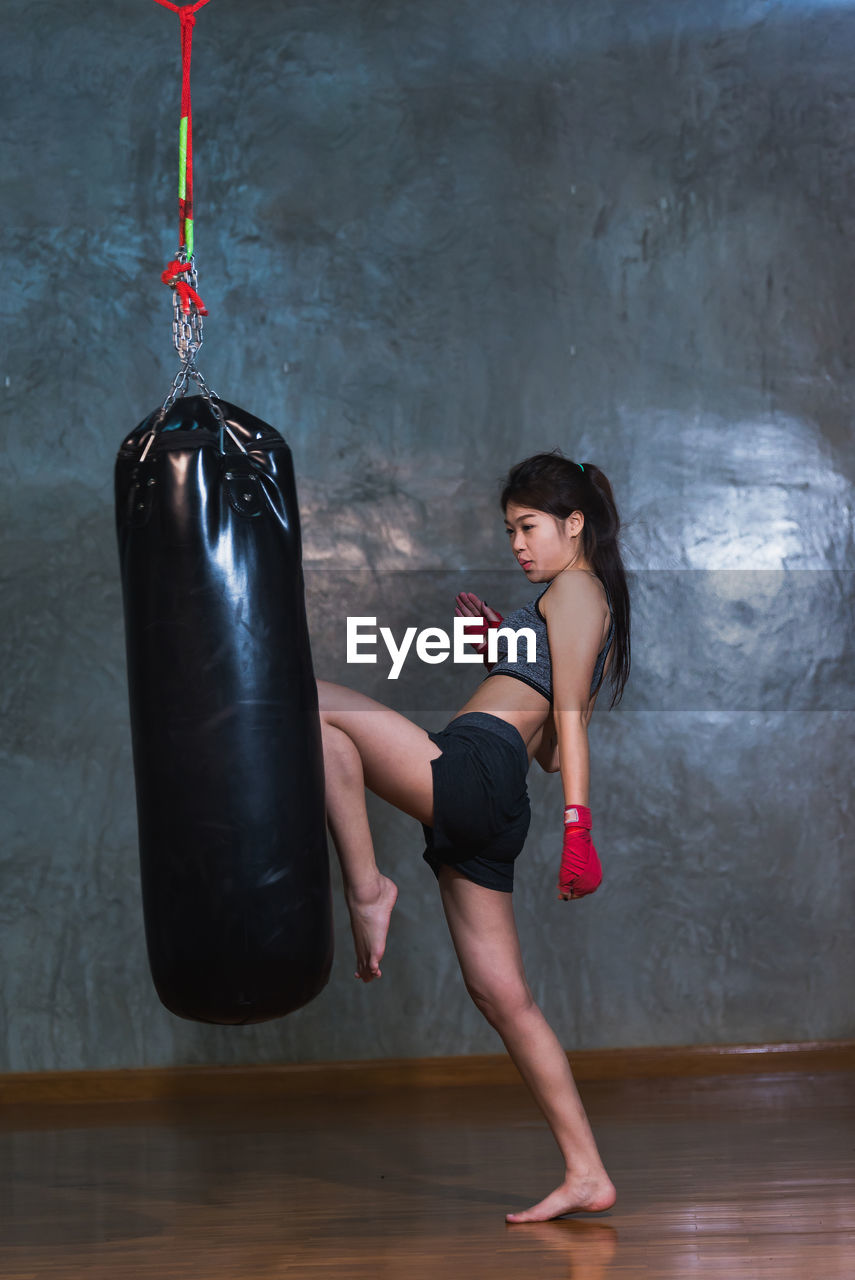 Full length of female boxer kicking punching bag