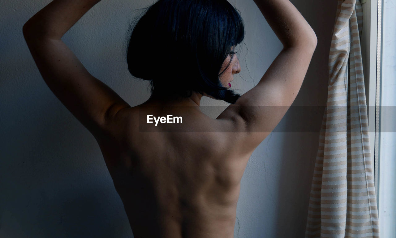 Rear view of shirtless woman standing at home