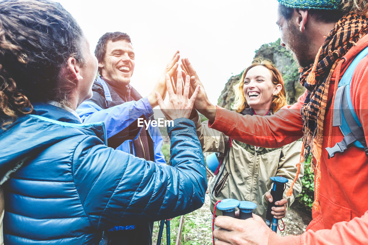 People laughing while giving high-five against sky