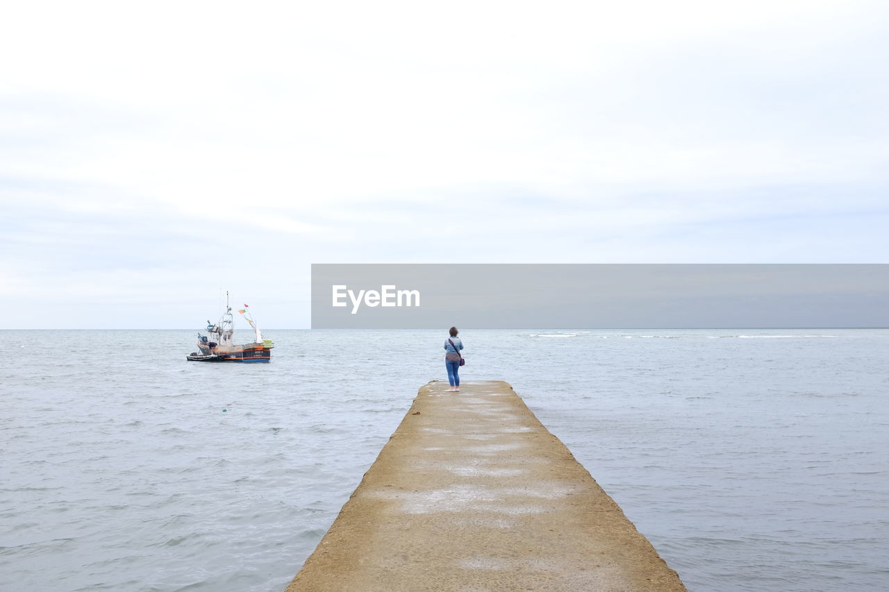 Woman standing on pier over sea against sky