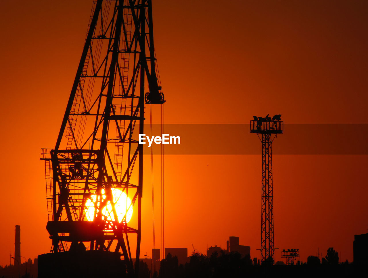 SILHOUETTE CRANES AGAINST SKY AT SUNSET
