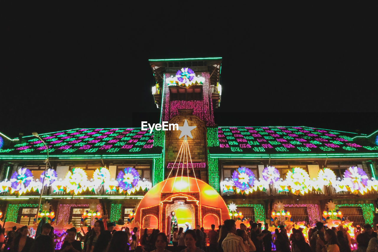 GROUP OF PEOPLE IN FRONT OF ILLUMINATED BUILDING