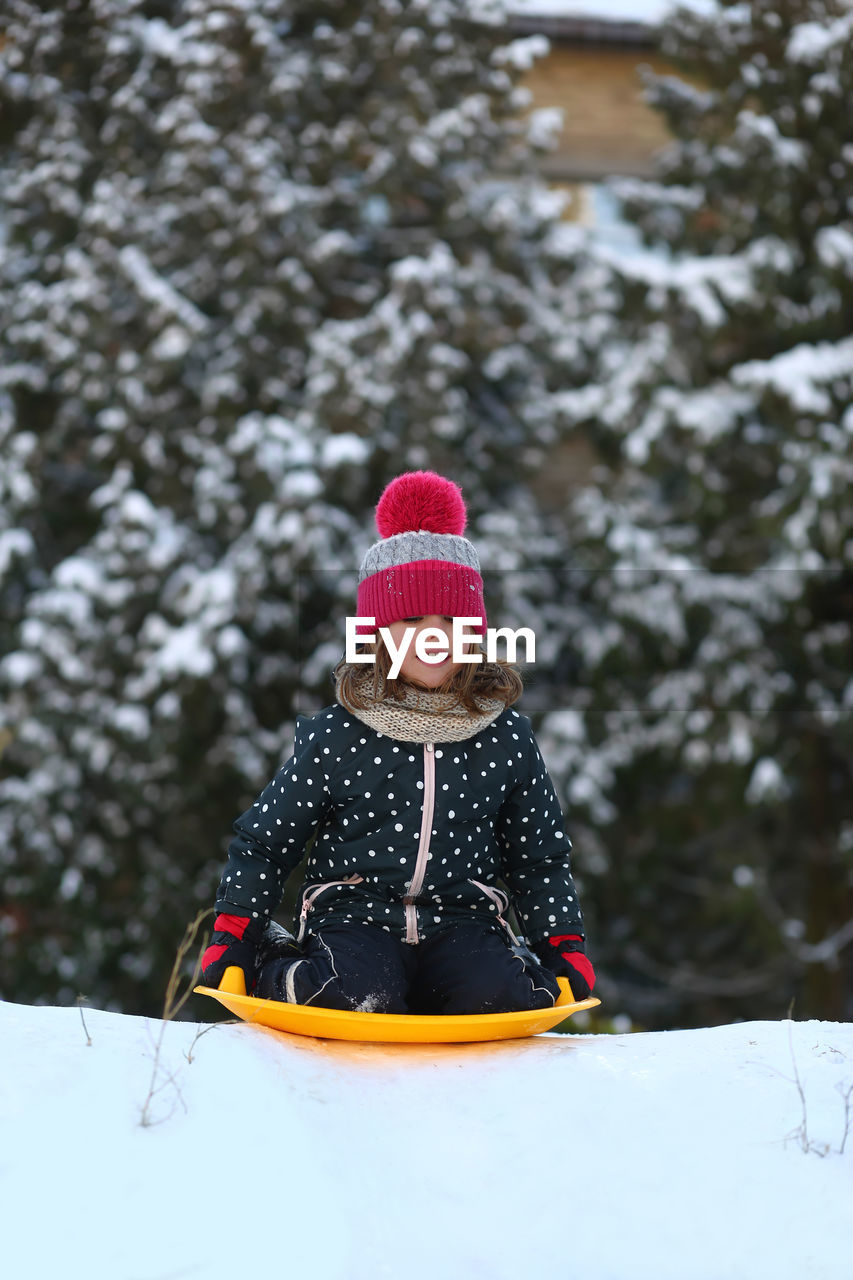 winter, snow, cold temperature, clothing, warm clothing, child, childhood, hat, one person, nature, happiness, leisure activity, fun, tree, knit hat, portrait, women, holiday, smiling, front view, enjoyment, female, glove, day, emotion, sled, toddler, plant, outdoors, mitten, vacation, trip, sitting, snowing, cheerful, land, tobogganing, looking at camera, lifestyles, forest, sports, adult
