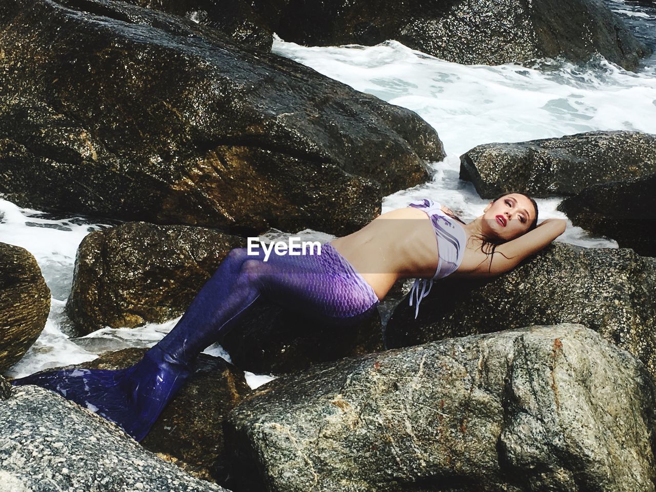 Young woman wearing mermaid costume while lying on rock near sea