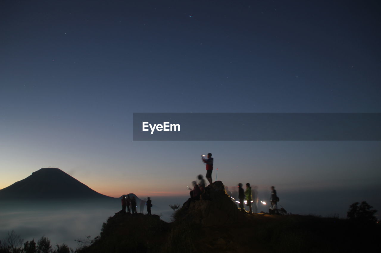 Silhouette people on mountain against clear sky