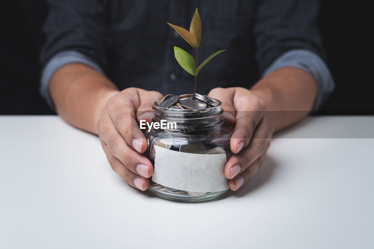 Close up hand of a man holding a glass jar with a coin inside concept of saving and investment