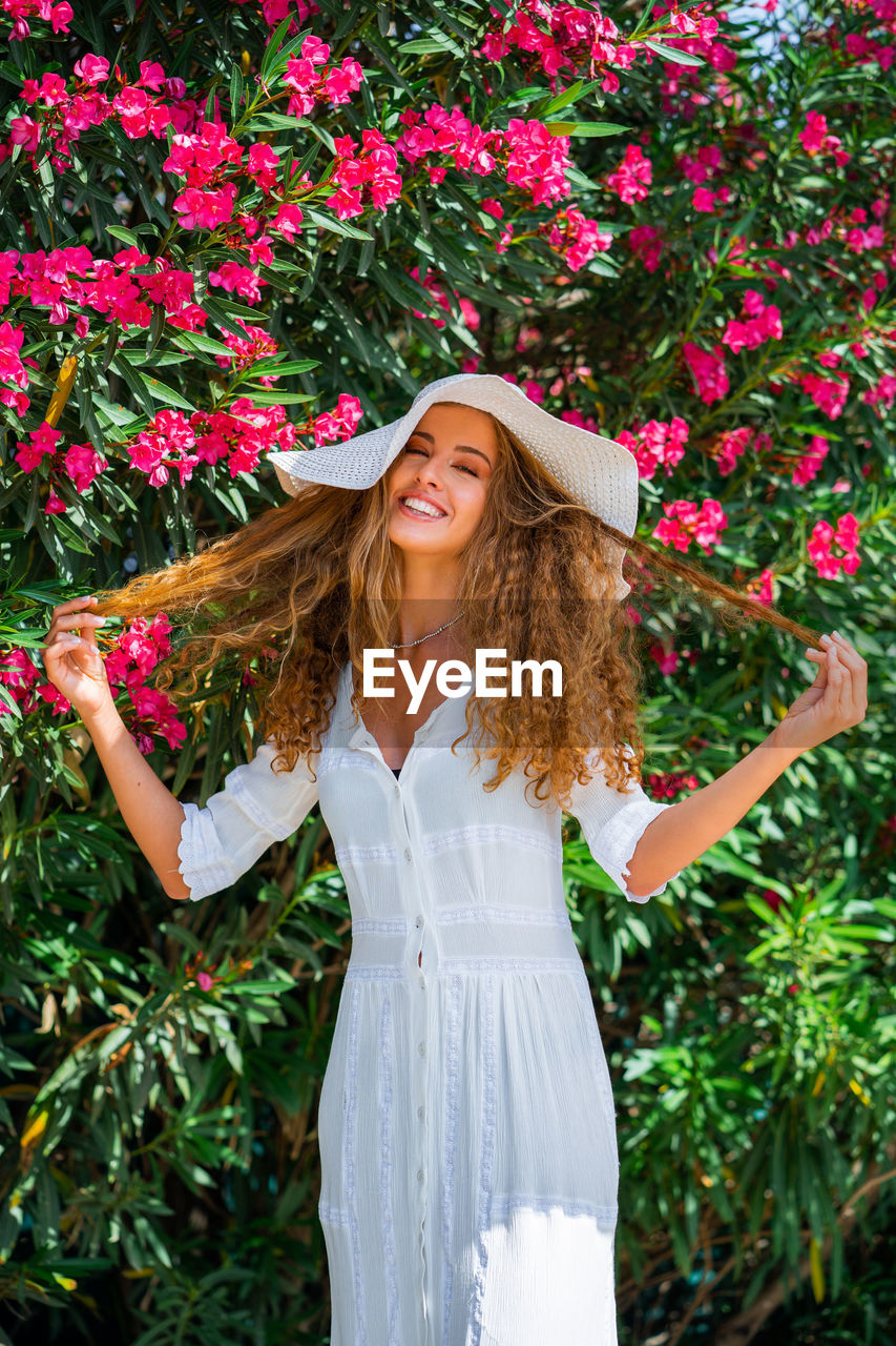 Portrait of a smiling young woman standing against plants and flowers, when it's summertime.