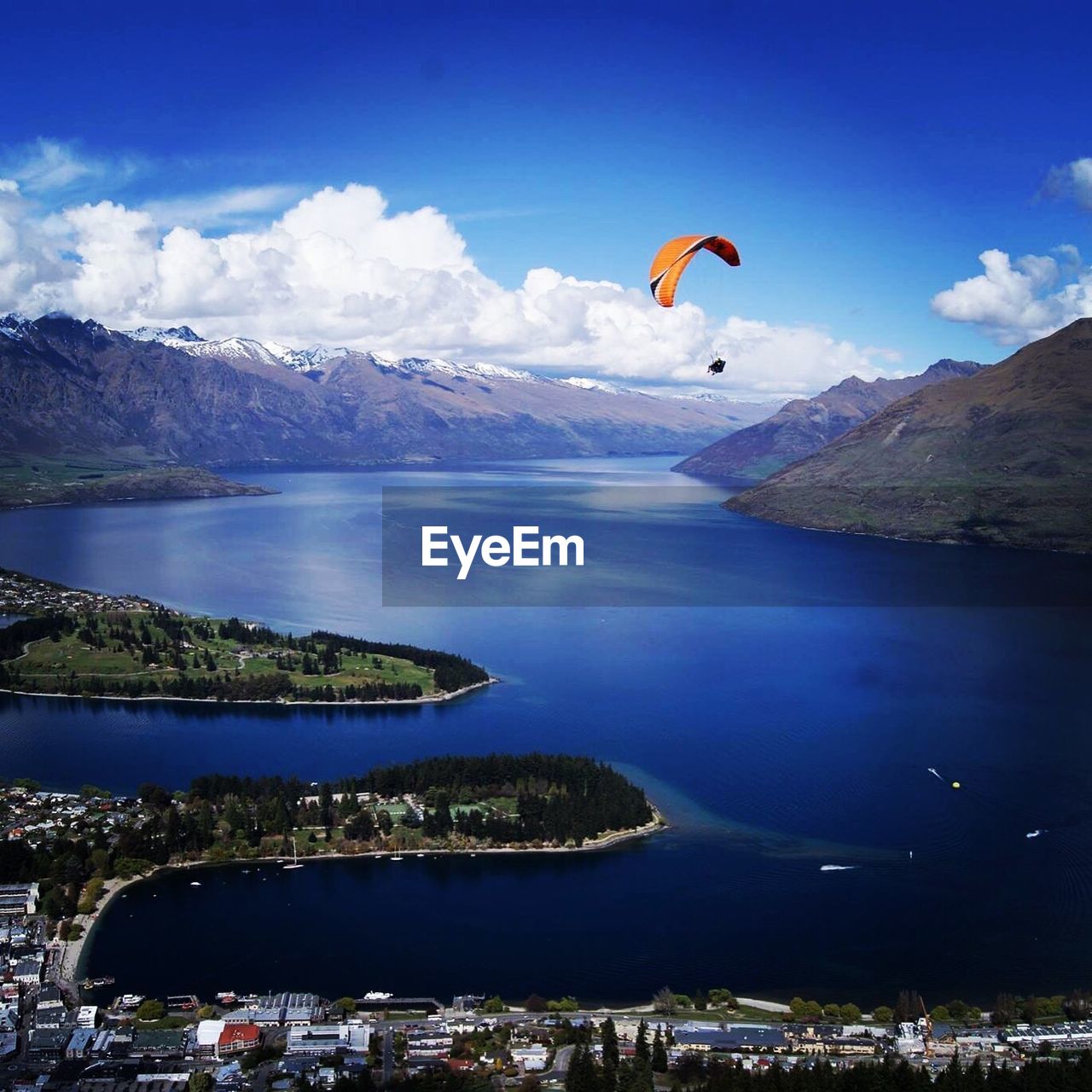 Low angle view of person paragliding over sea by city and mountains against sky