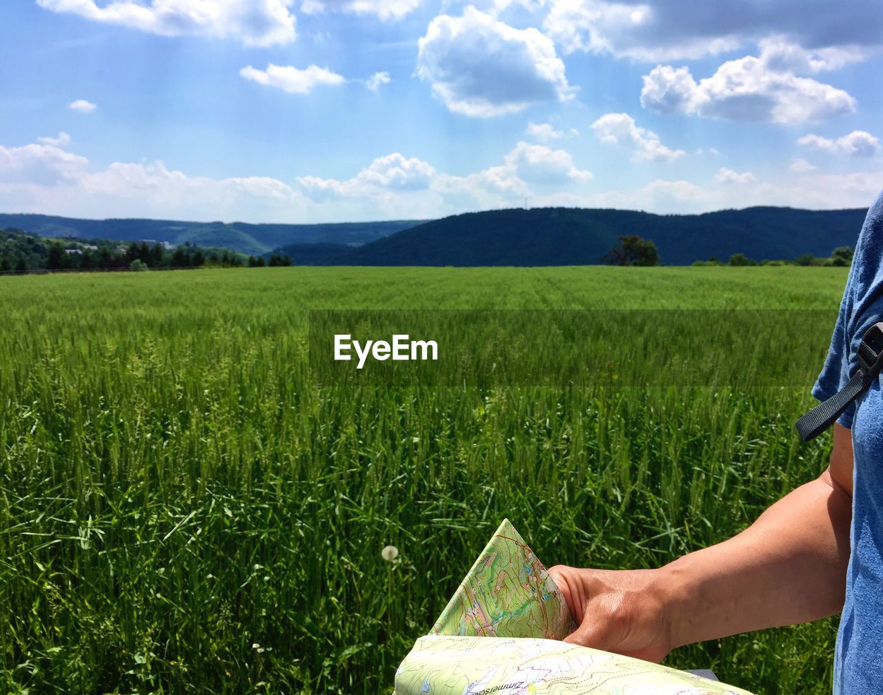 Midsection of man holding map on grassy landscape during sunny day