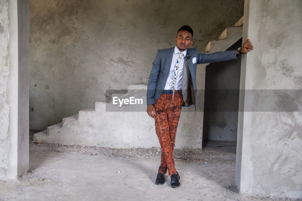 PORTRAIT OF SMILING YOUNG MAN STANDING AGAINST WALL