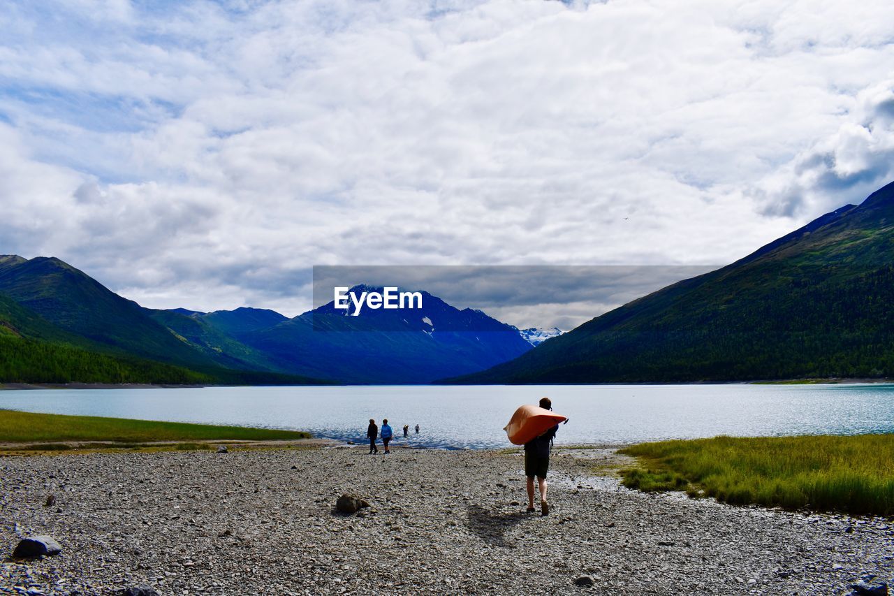 Rear view of men by lake against sky