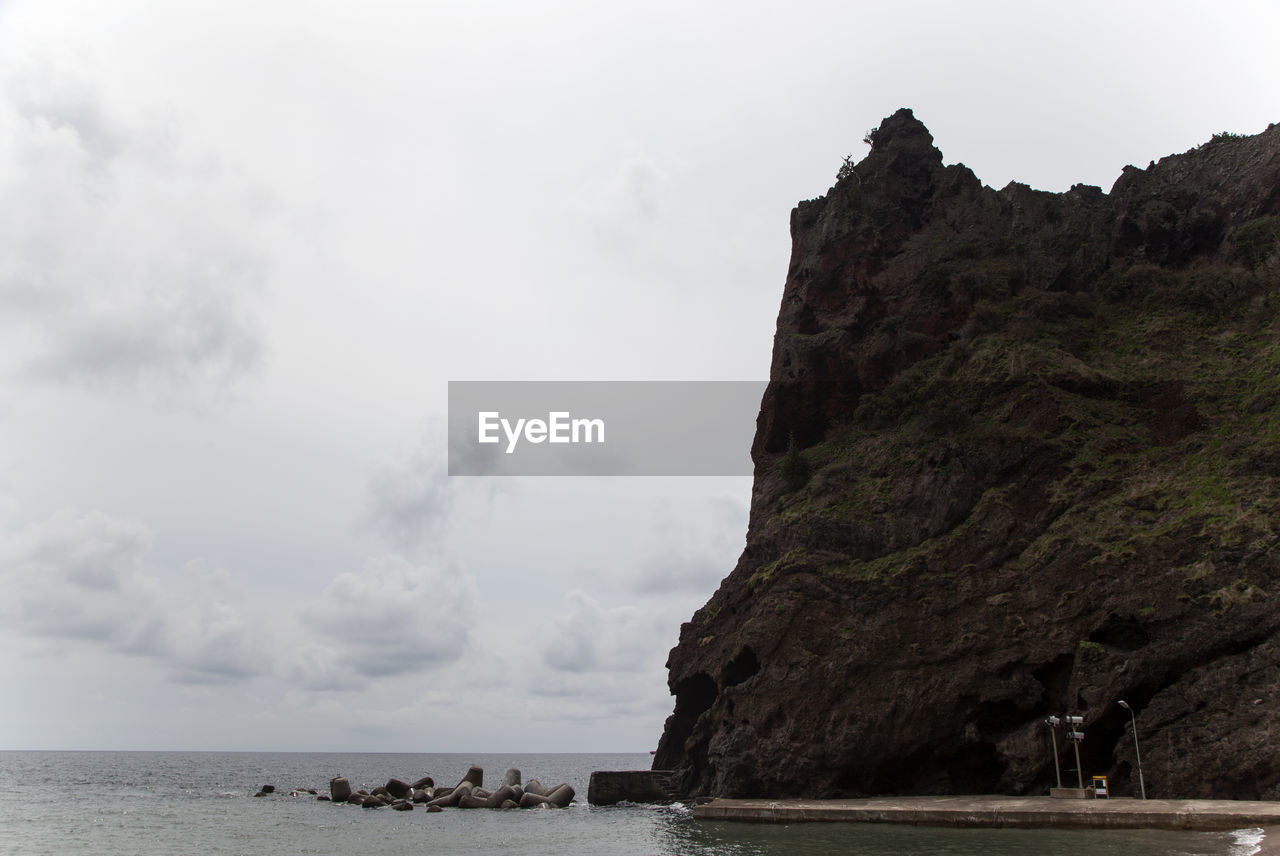 Scenic view of sea by mountain against cloudy sky