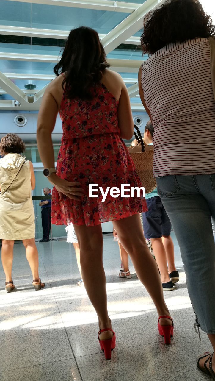 REAR VIEW LOW SECTION OF WOMEN STANDING IN CORRIDOR