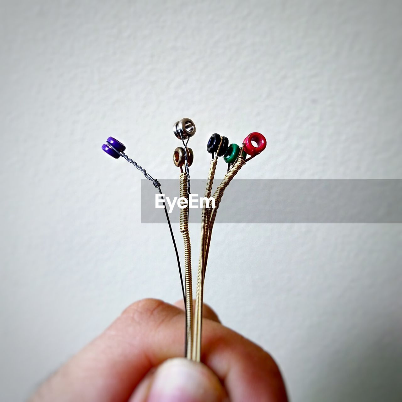 Cropped image of person holding guitar strings against wall