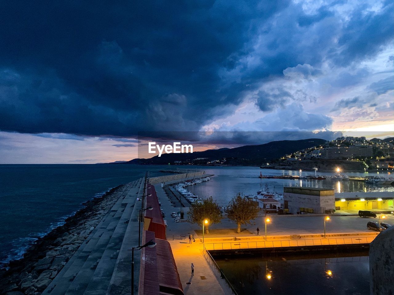 Illuminated city by sea against sky at night