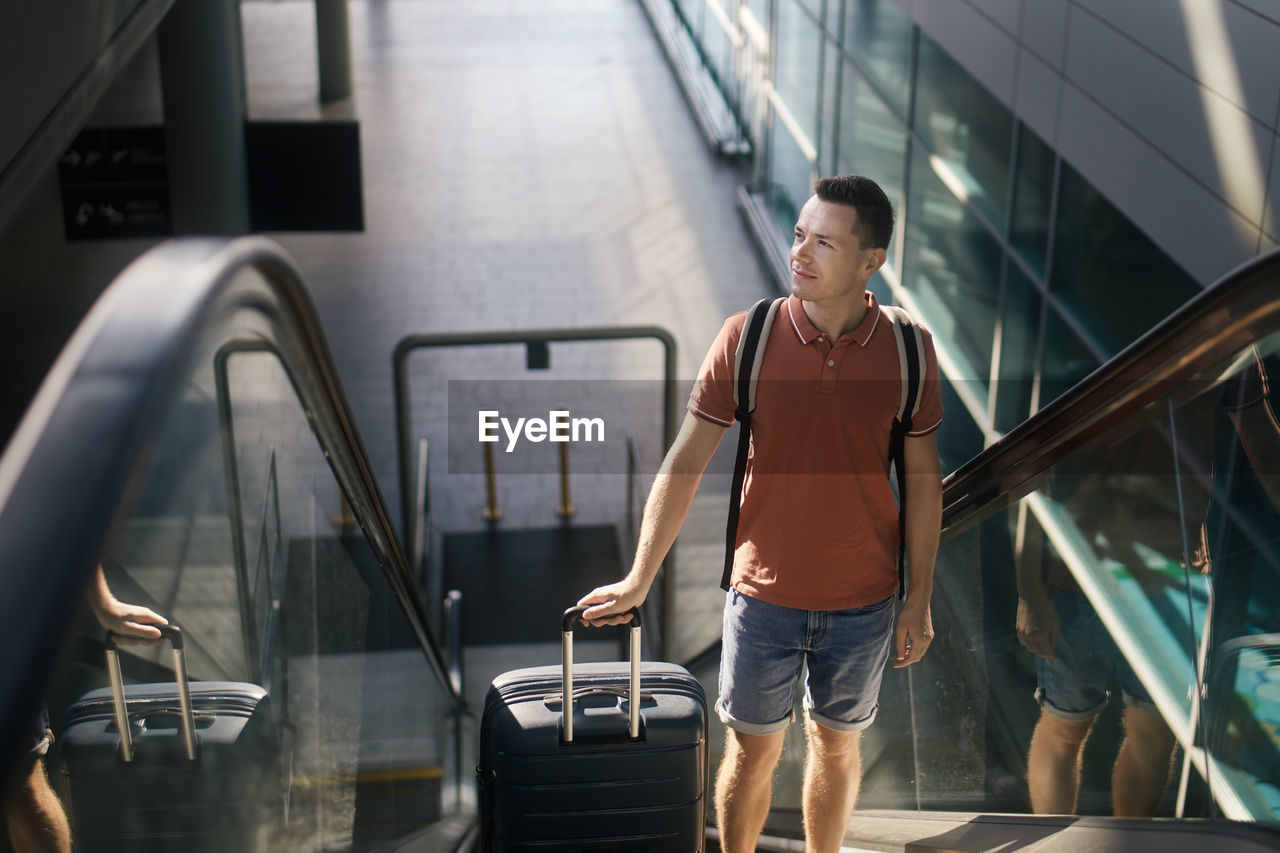 Traveler walking through airport terminal. man with suitcase standing on ecalator. 