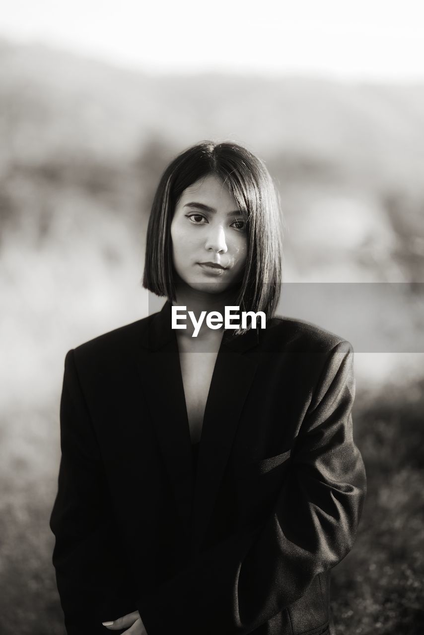 Portrait of young woman standing against trees