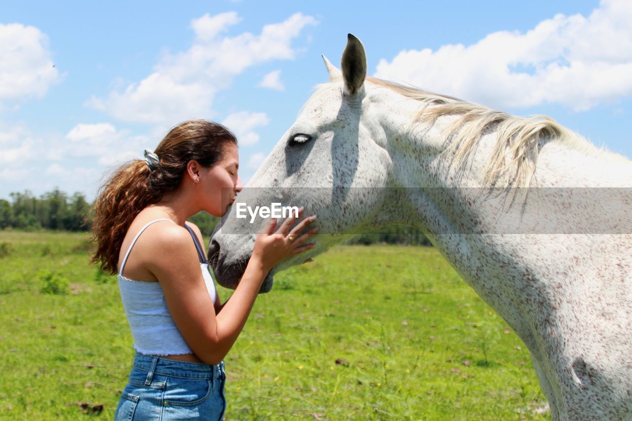 Side view of woman kissing horse at farm