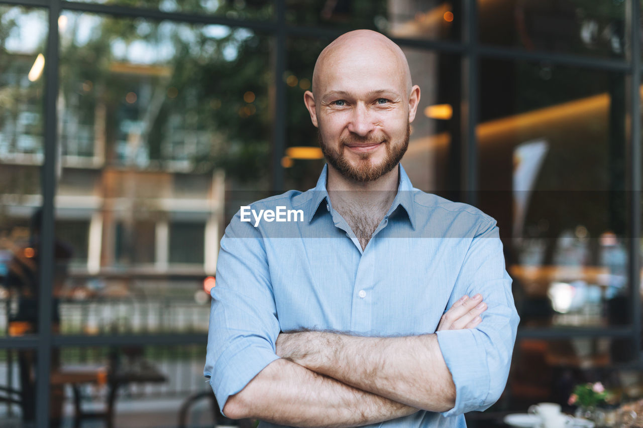  adult smiling attractive man forty years with beard in blue shirt businessman against glass wall 