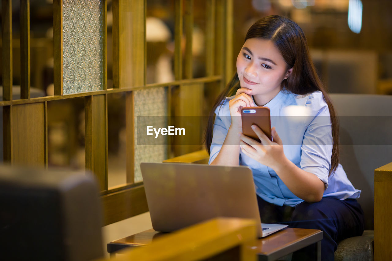 Smiling businesswoman using mobile phone while sitting in cafe at night