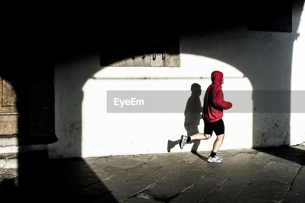 Full length side view of man jogging against white wall