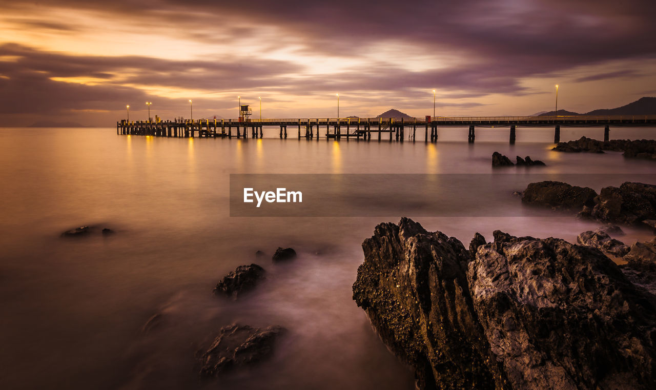 Jetty at calm sea against clouds