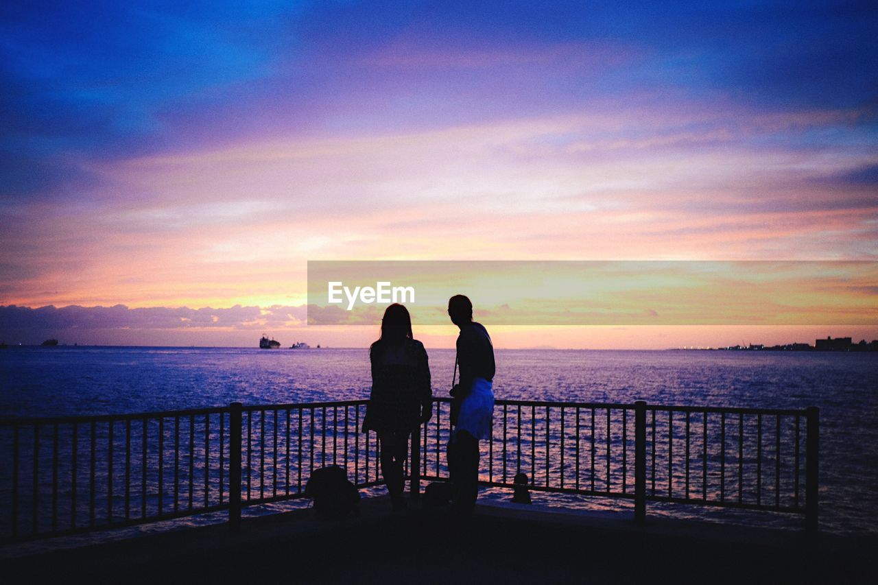 Couple standing on pier looking at sea