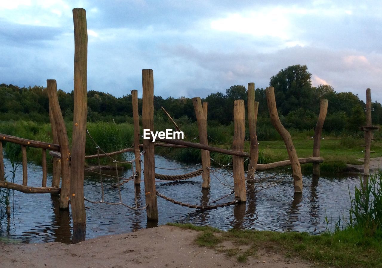 WOODEN POSTS IN SEA AGAINST CLOUDY SKY