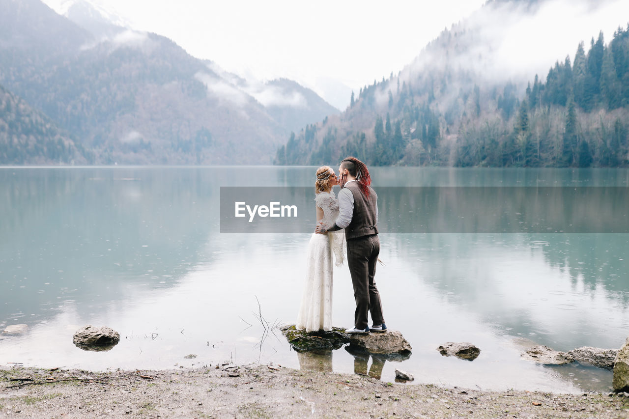 Happy newlyweds in love a man and a woman in wedding clothes embrace on the shore of the lake