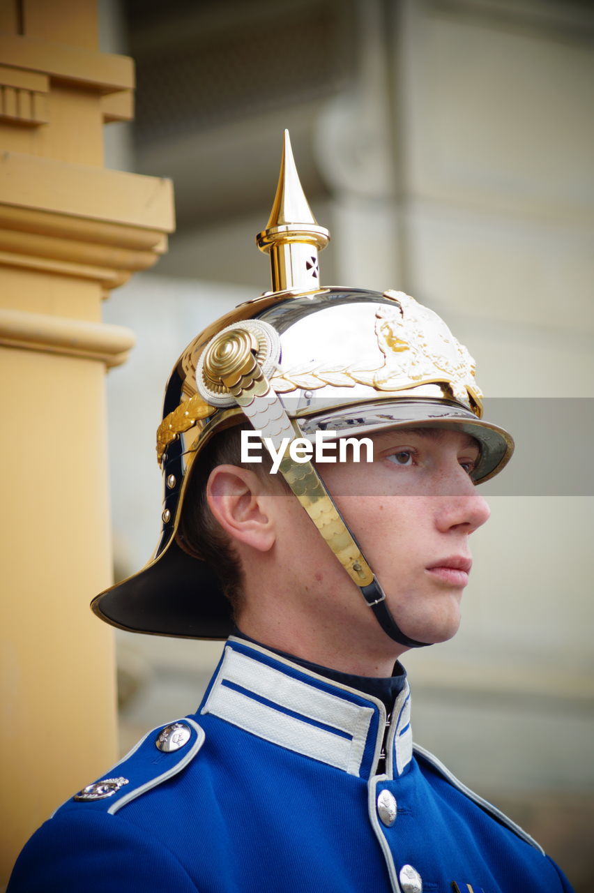 Low angle view of security guard in uniform looking away while standing against building