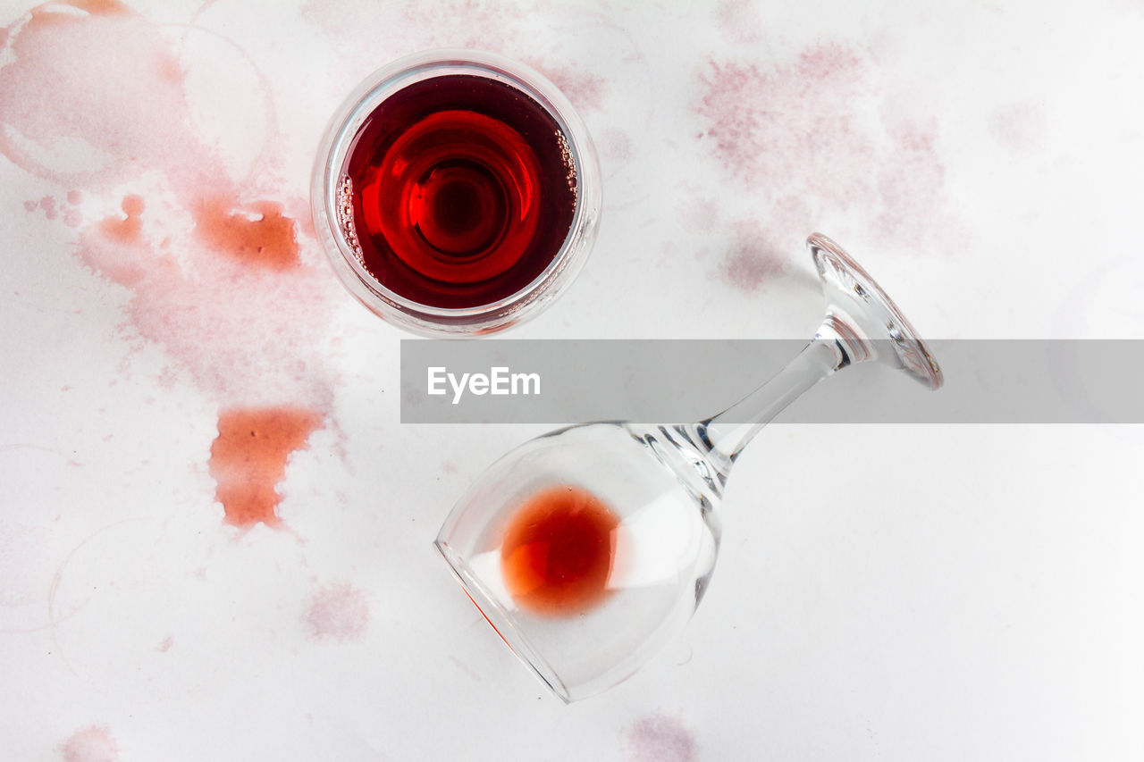 Glass of red wine and overturned glass with leftover wine on a white background