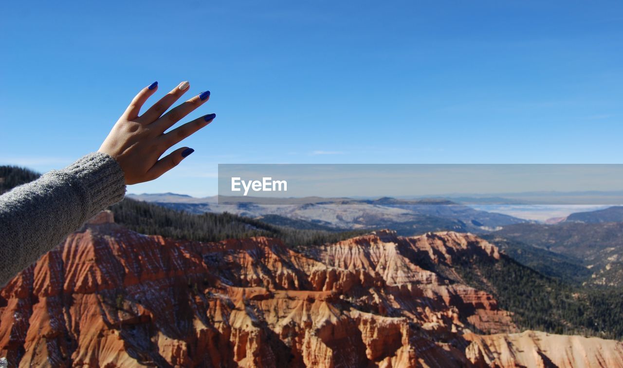 Cropped hand of woman reaching sky over mountains