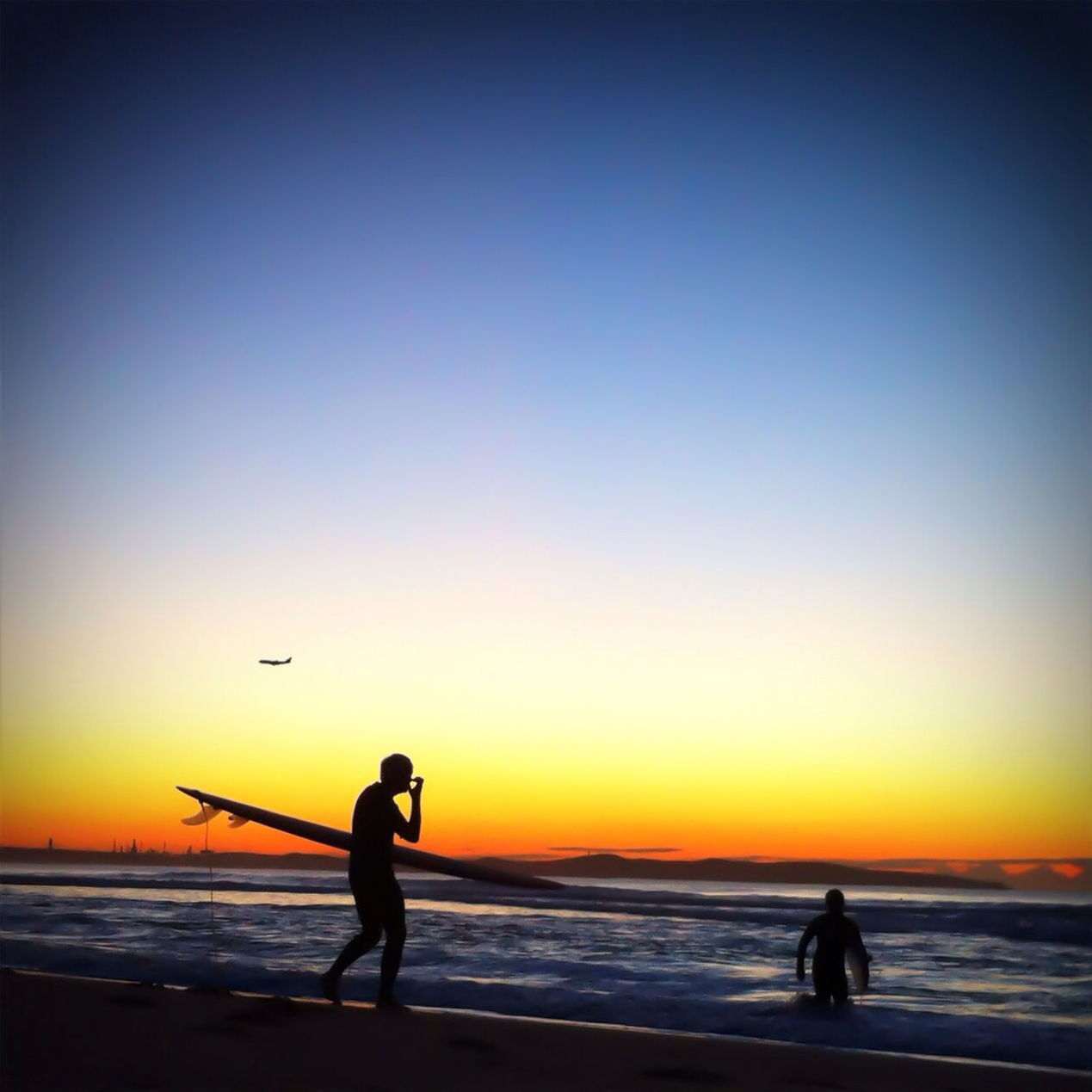 Two silhouette men with surfboards on beach at sunset