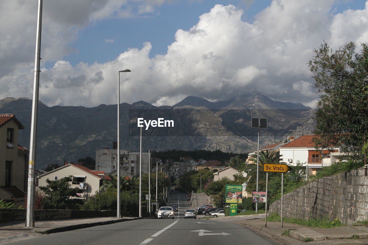 Road by buildings and mountains against sky