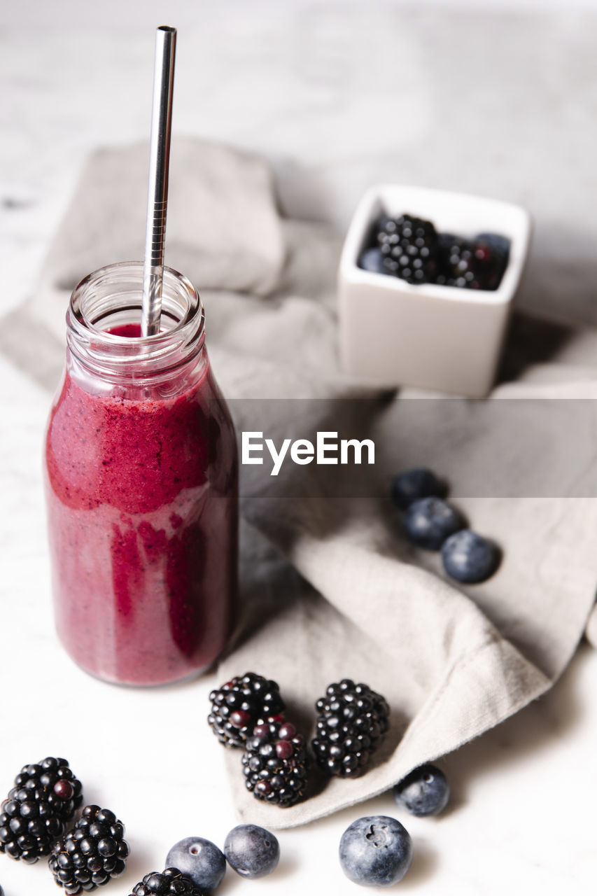 Pink vegan smoothie, berries and a metal straw on a marble surface. vertical image.