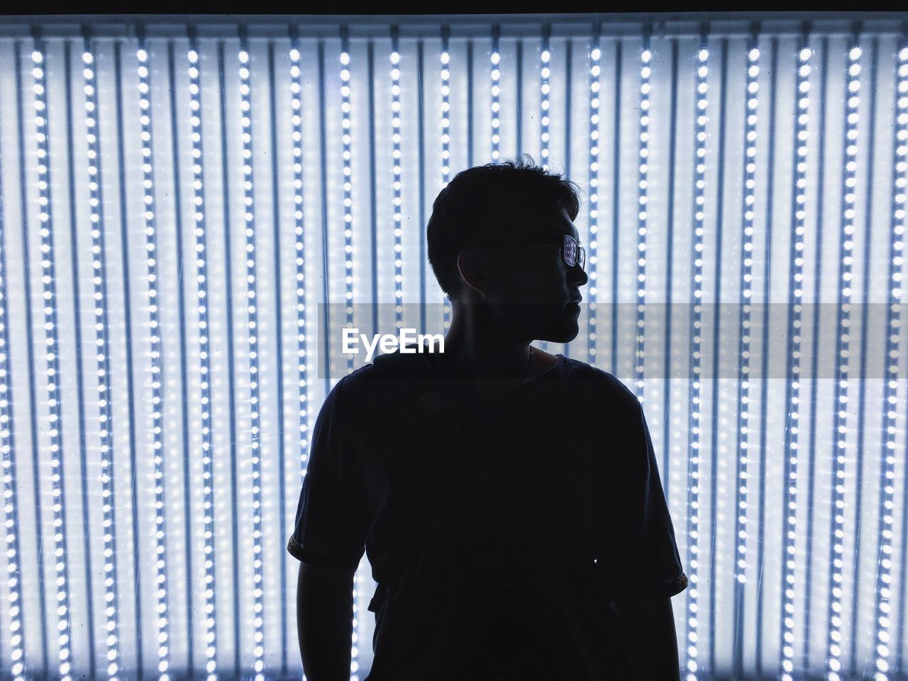 Man with sunglasses standing against illuminated wall