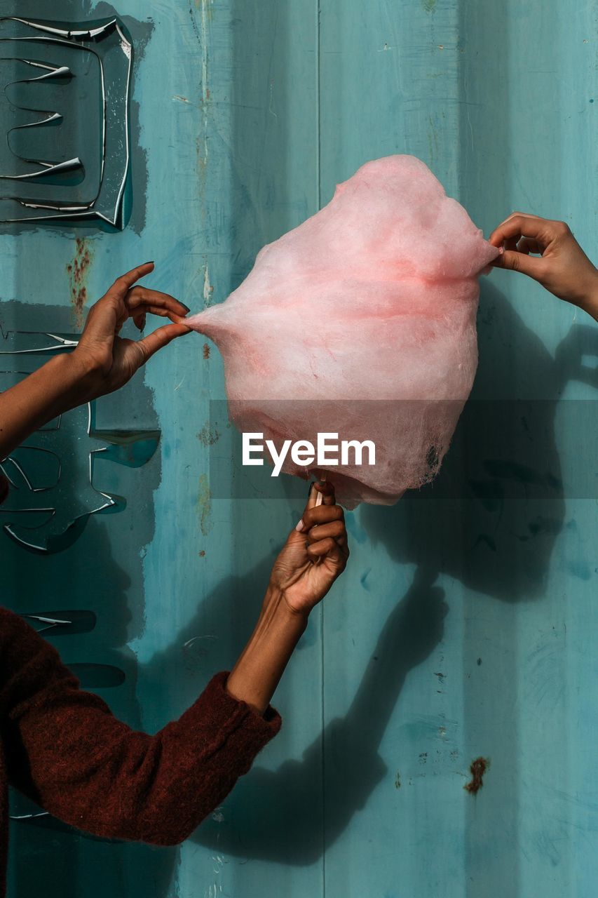Cropped image of people holding cotton candy against corrugated iron
