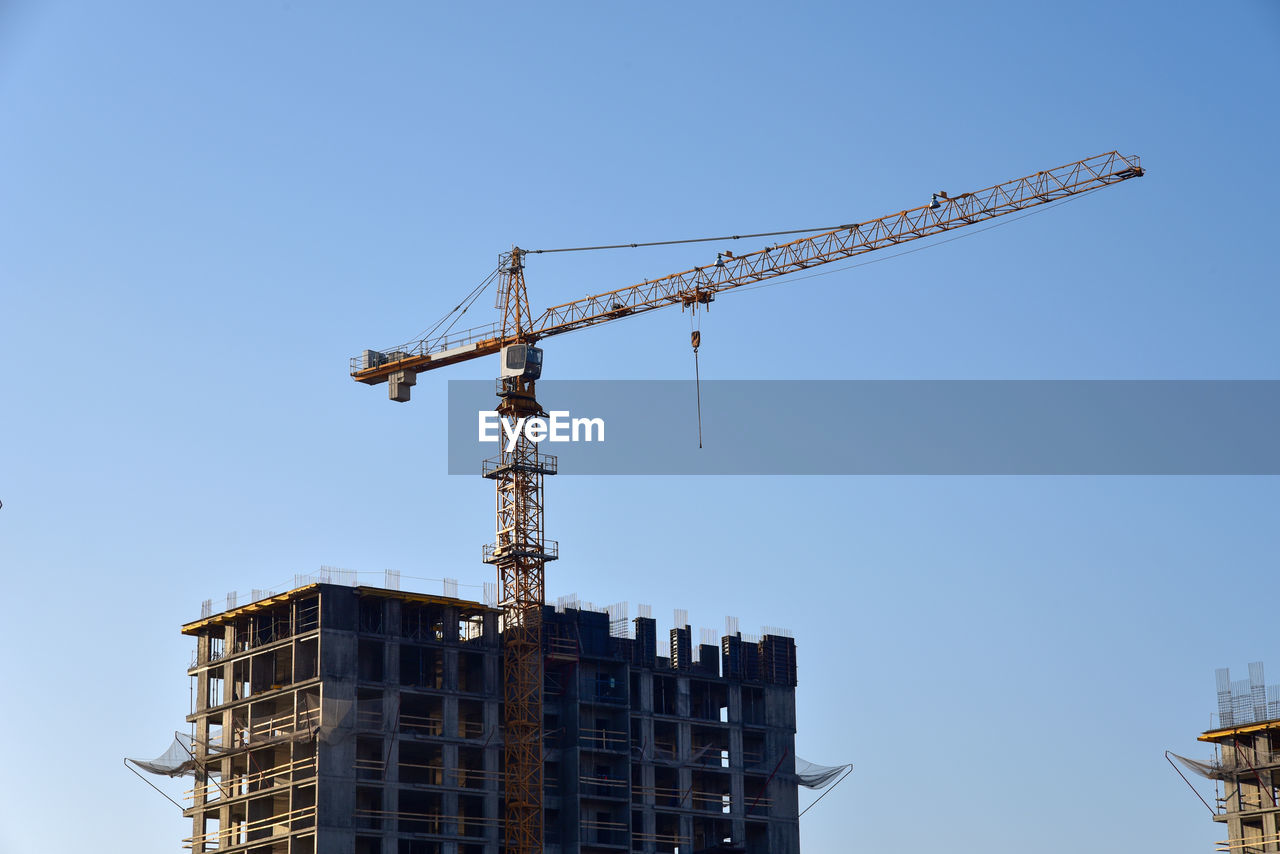 Low angle view of crane on building against clear blue sky