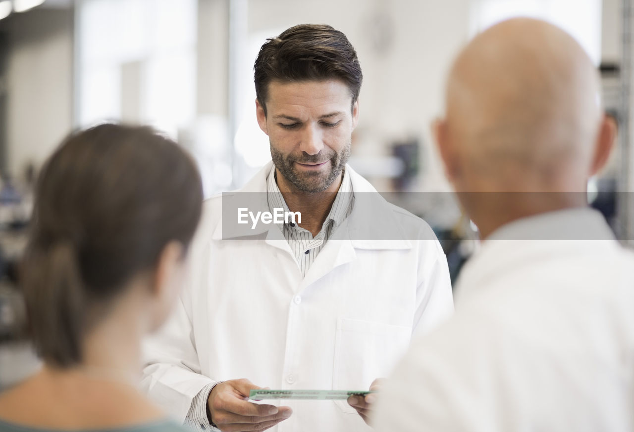 Engineer looking circuit board with business people in foreground at manufacturing plant