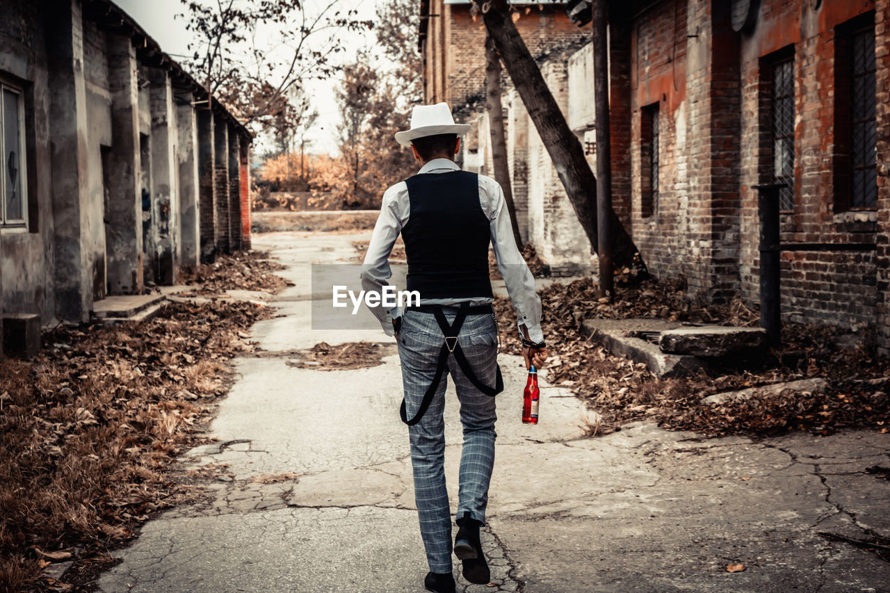 Rear view of a man holding beer bottle while walking through town street.