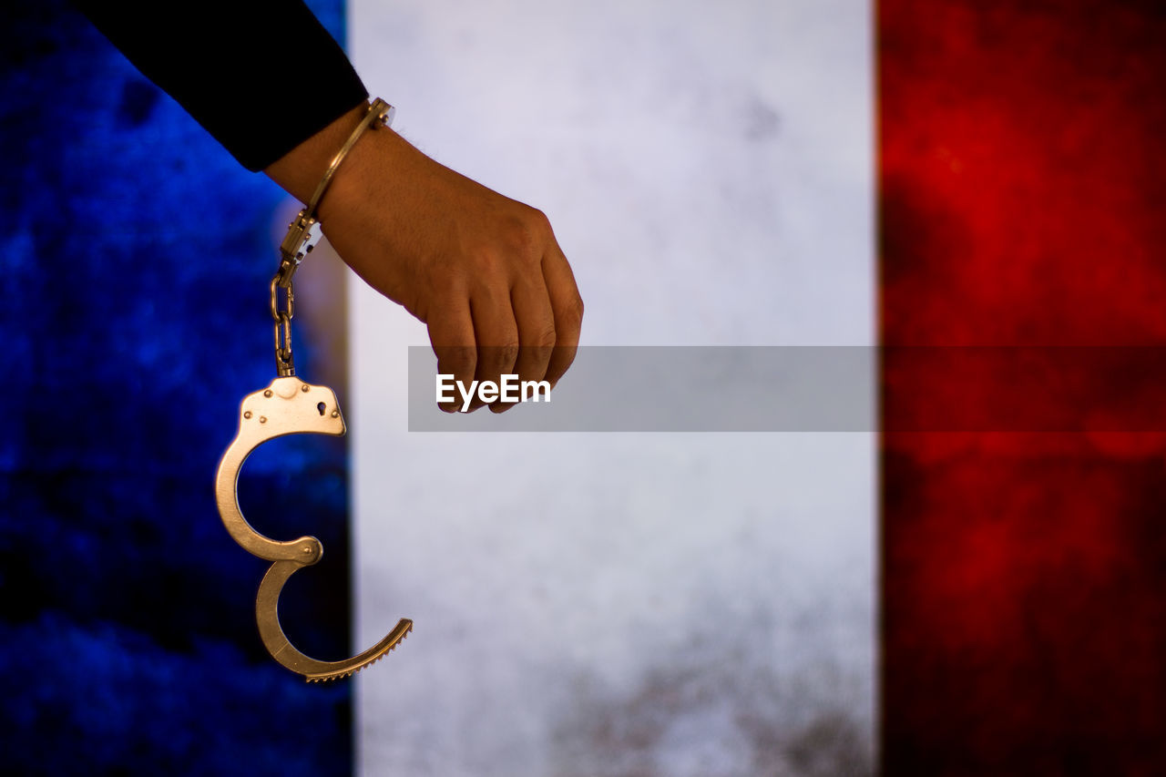 Cropped hand of male criminal with handcuffs against french flag