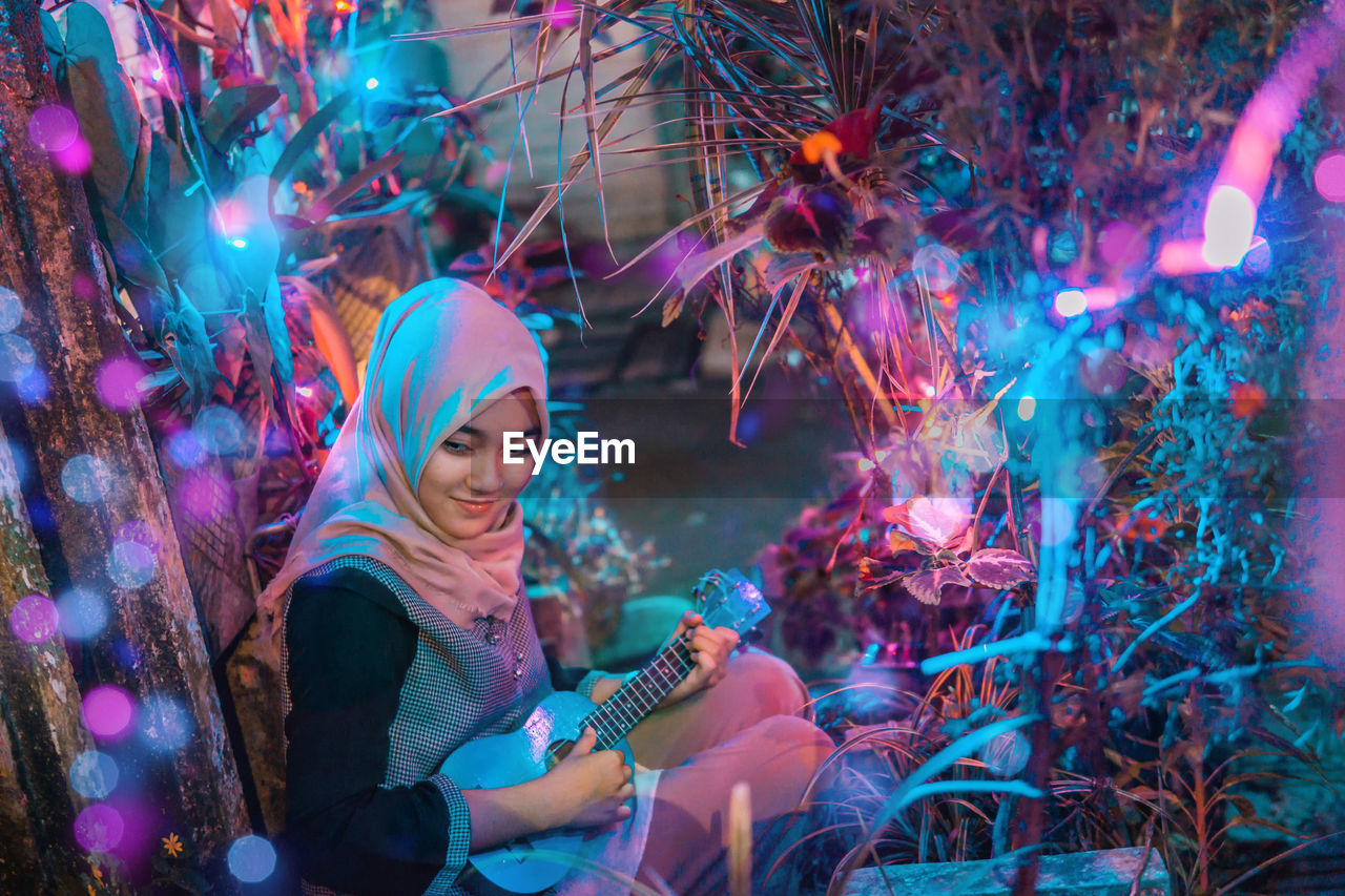 Young woman playing guitar amidst illuminated decorations