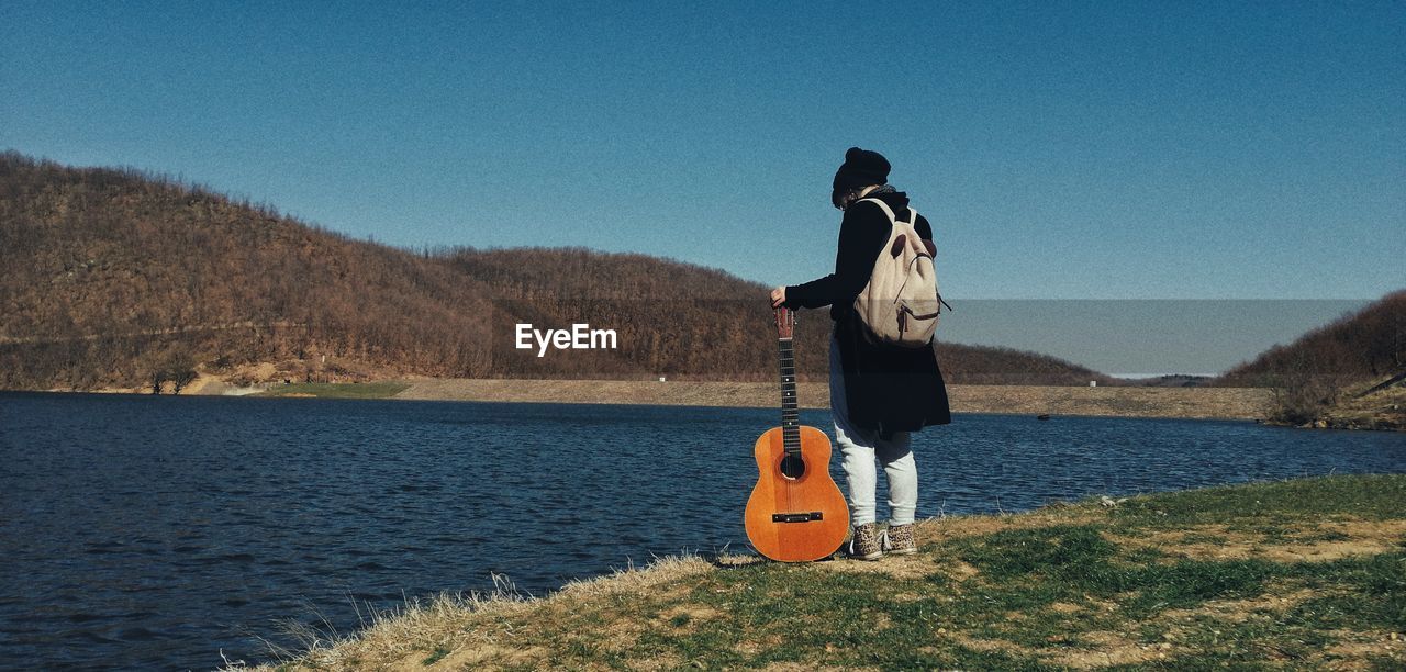 Rear view of woman standing by lake against sky