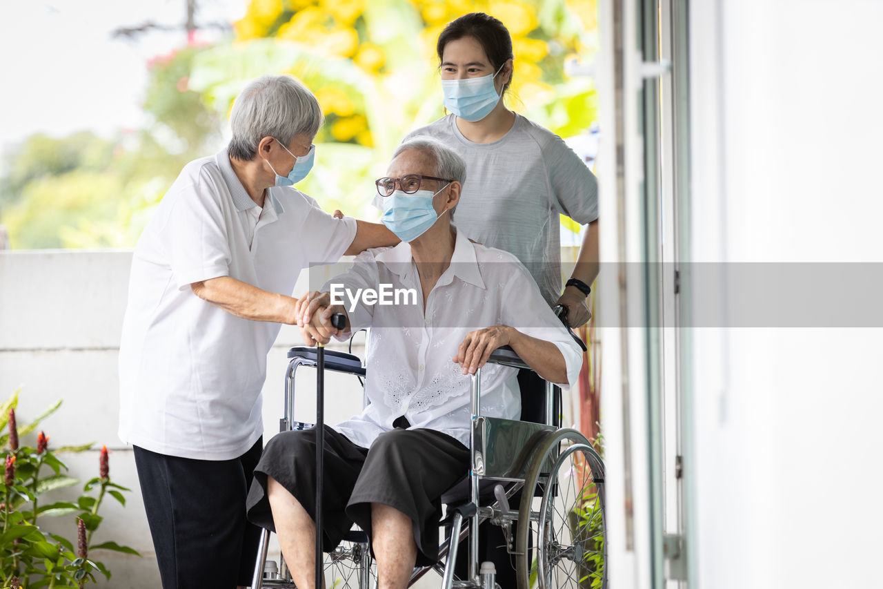 People standing by man sitting on wheelchair wearing mask