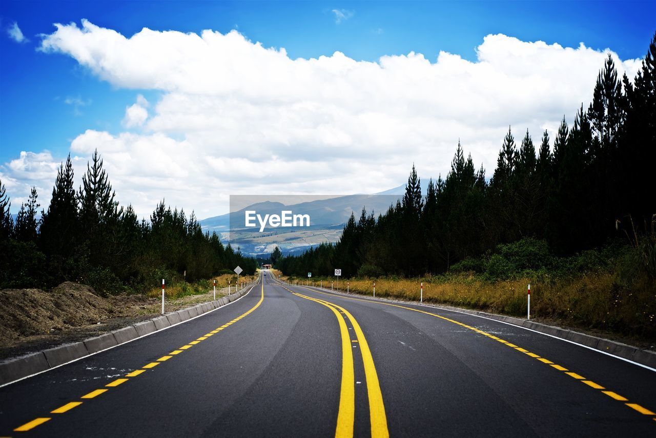 Empty road along trees and mountains against sky