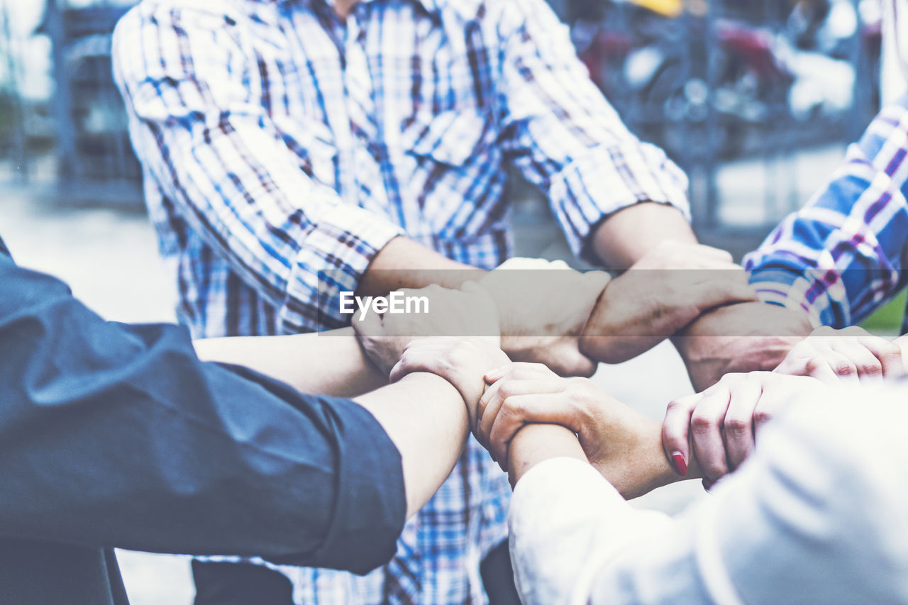 Close-up of friends holding hands while huddling outdoors