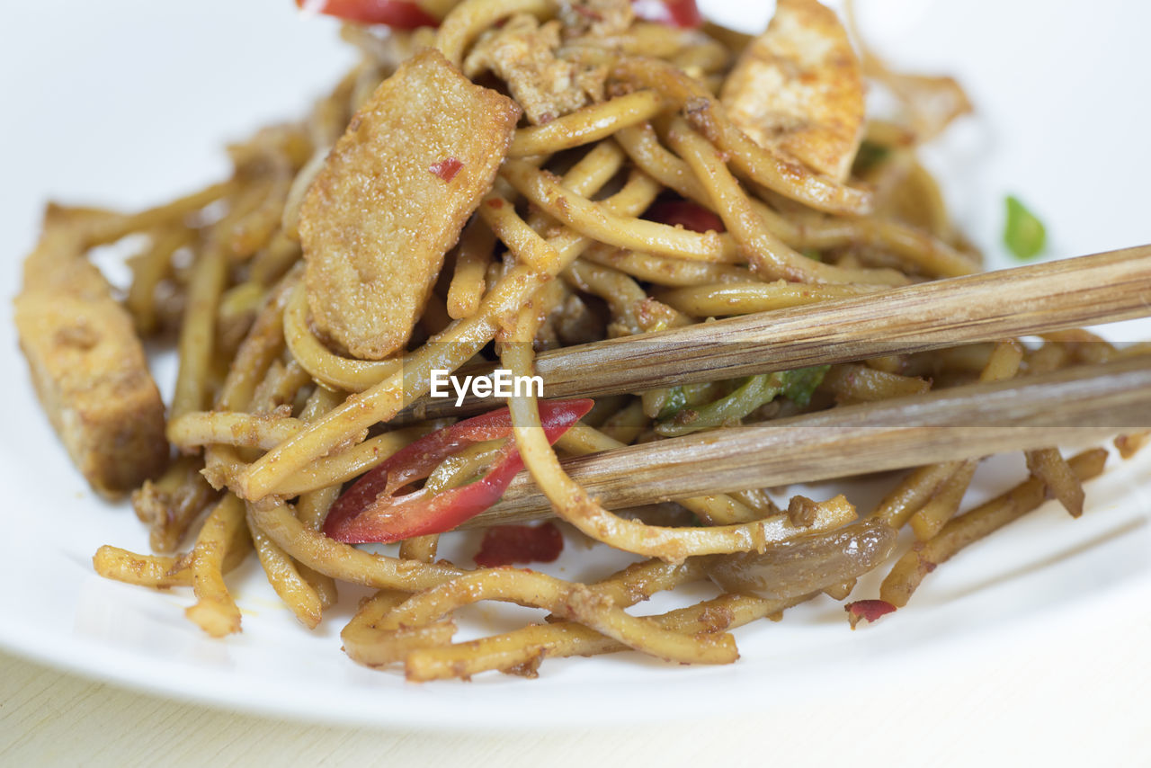 CLOSE-UP OF NOODLES IN PLATE WITH FORK AND SAUCE IN TRAY