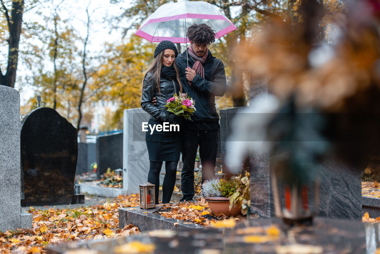 Couple standing with umbrella at cemetery